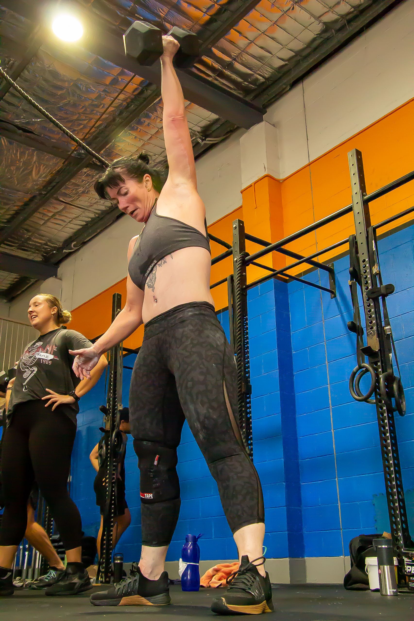 Athlete performing an overhead stretch during a workout in a CrossFit gym.