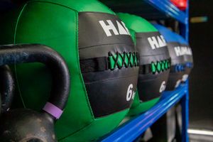 Row of green and black weighted fitness bags arranged on blue storage shelves.