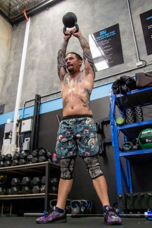 Athletic person performing kettlebell exercises in camouflage shorts at a gym.