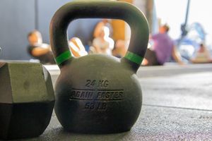 Kettlebells lined up on a gym floor with blue equipment racks in the background.