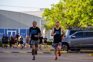 Two runners competing in an outdoor race through a parking lot.