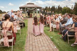 A wedding ceremony taking place outdoors with guests seated along a brick pathway leading to a gazebo.