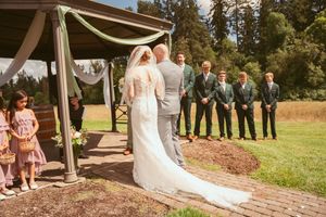 A wedding ceremony taking place under a wooden gazebo decorated with white fabric on a beautiful sunny day.