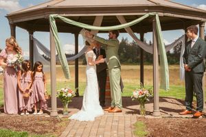 An outdoor wedding ceremony in a gazebo with sage green decor and pink floral arrangements.