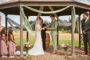 A wedding ceremony in progress under a decorated gazebo with mint green fabric draping and floral arrangements.
