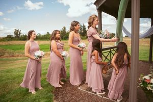 Bridesmaids in dusty rose dresses gather during an outdoor wedding ceremony under a gazebo.