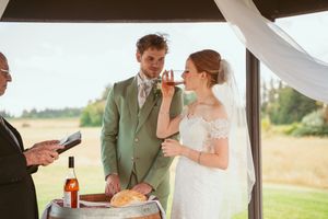 Wine is poured from a bottle into glasses on top of a wooden barrel during an outdoor wedding celebration.