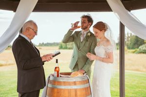Wedding party gathers around a rustic wine barrel during an outdoor celebration.