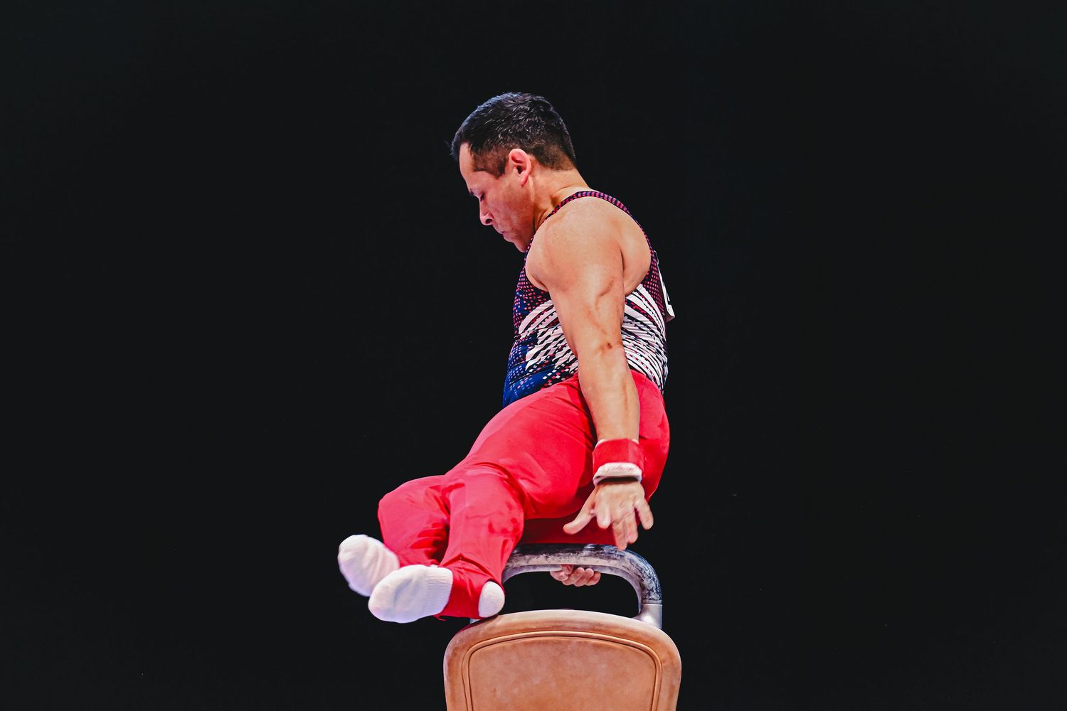 Athletes perform impressive gymnastic moves on parallel bars in a dark indoor gymnasium setting.