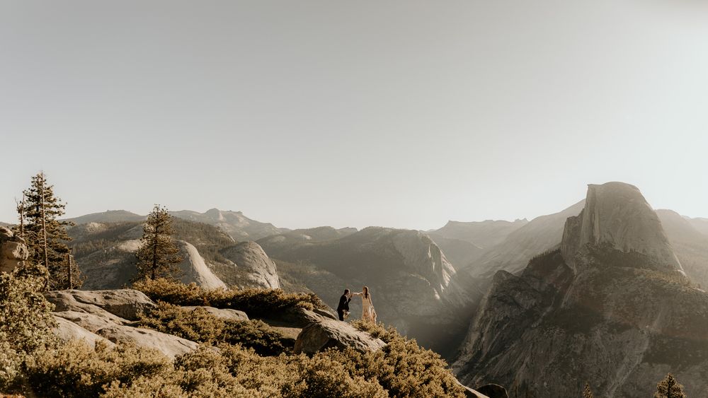 Panoramic mountain vista with distant figures on rocky outcrop at sunset.