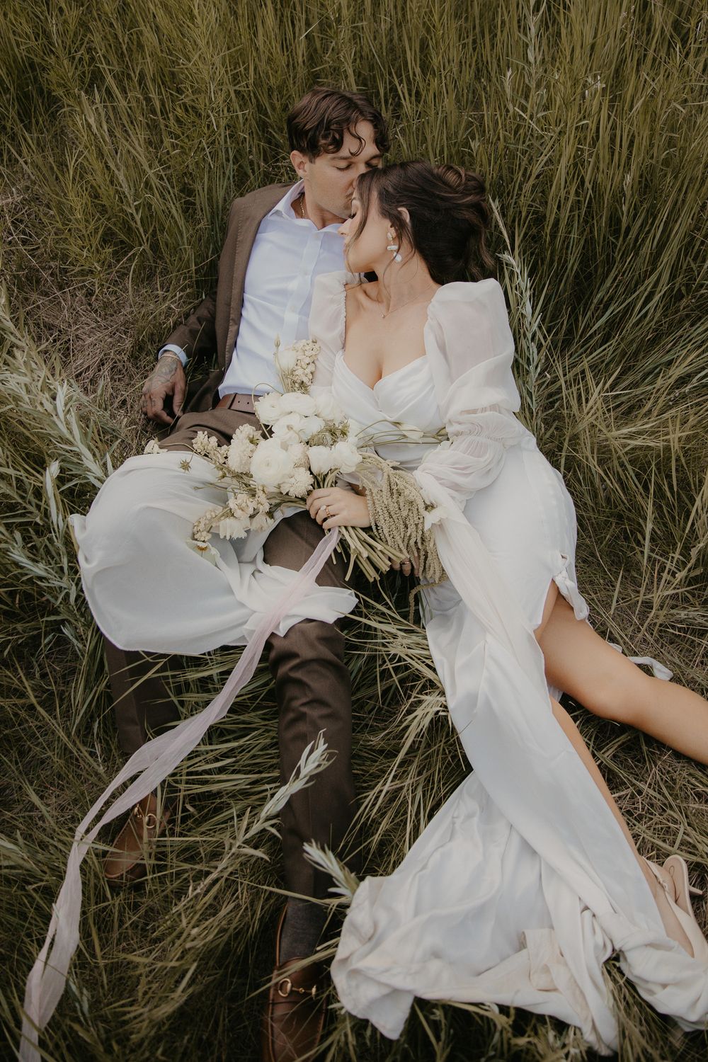 Ethereal bridal portrait in flowing white dress against tall grass field.