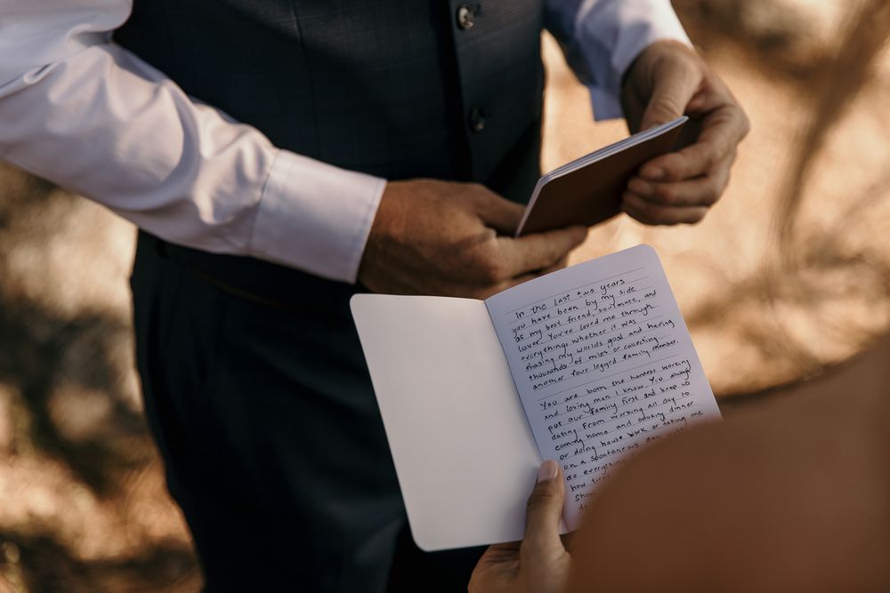 Close-up shot of hands holding handwritten vows on paper during an outdoor ceremony.