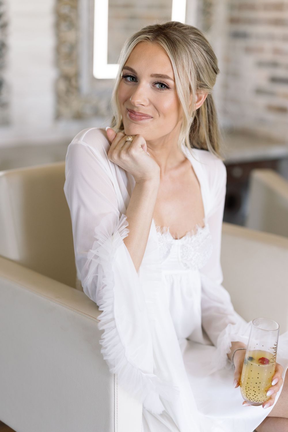 Woman in white dress holds refreshing iced beverage while sitting in bright modern interior.