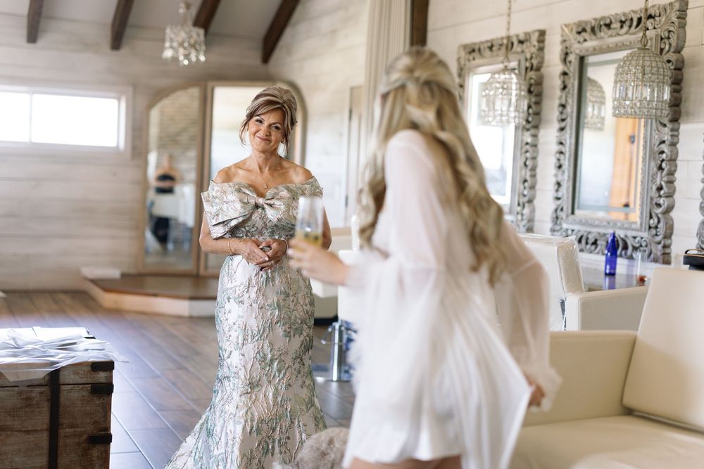 Two people in wedding attire sharing an emotional moment in a bright rustic room with ornate mirrors.