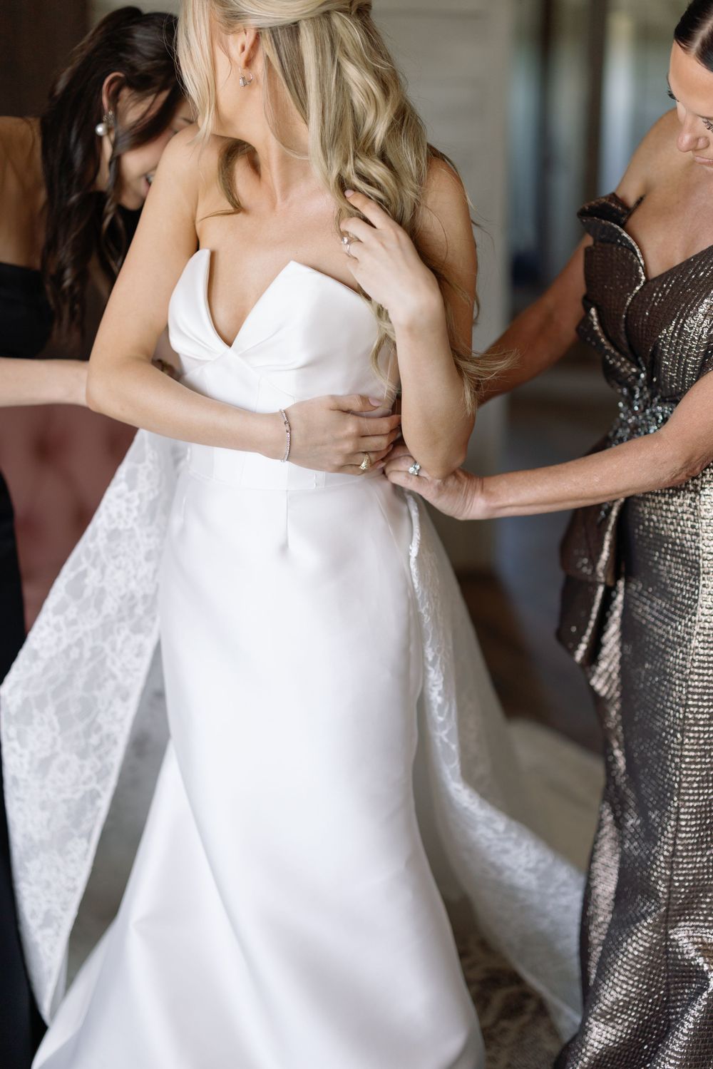 A bride in a white wedding dress embraces and dances with guests wearing silver sequined dresses during a celebration.