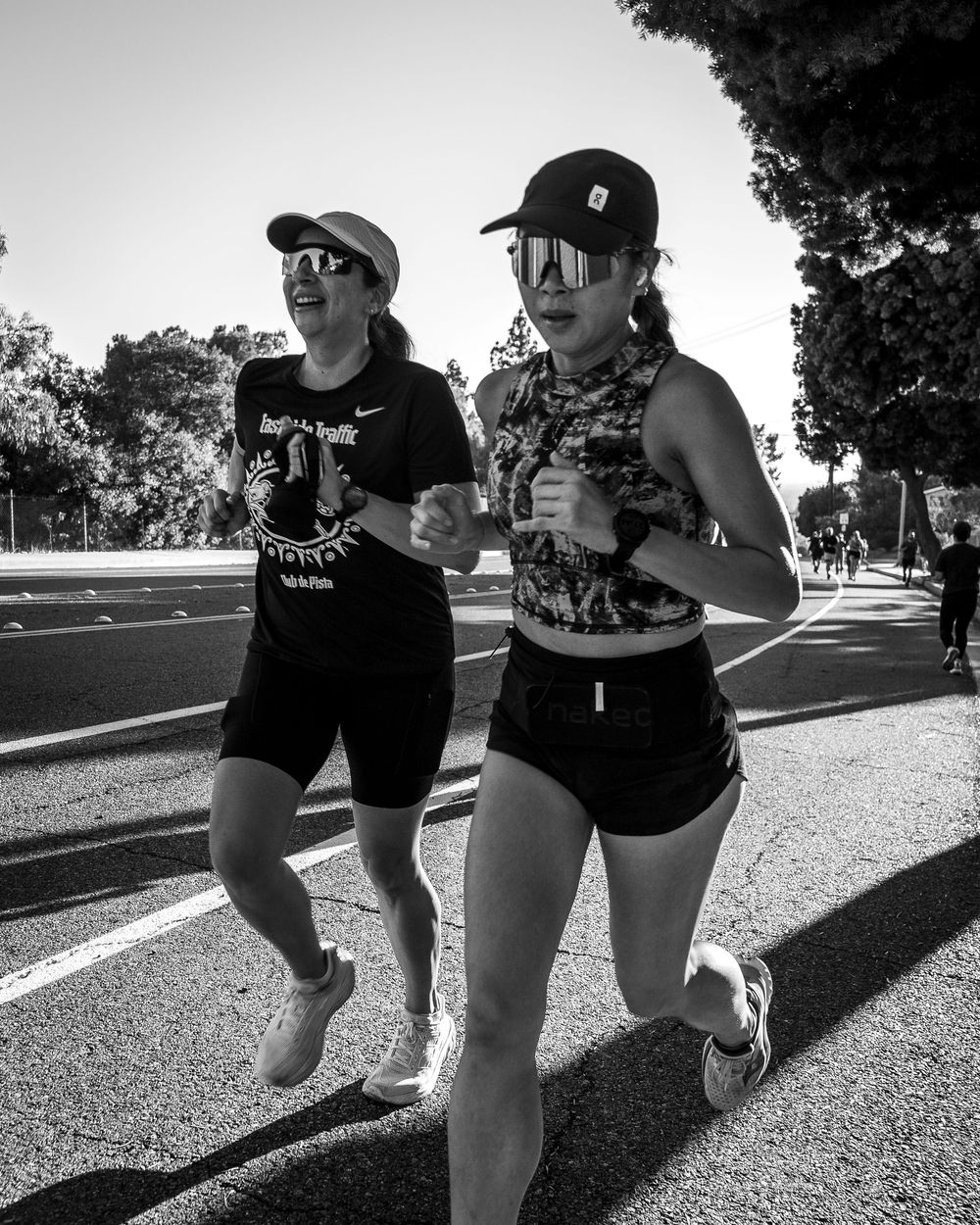 Black-and-white close-up of two runners in caps jogging on a sunlit road.