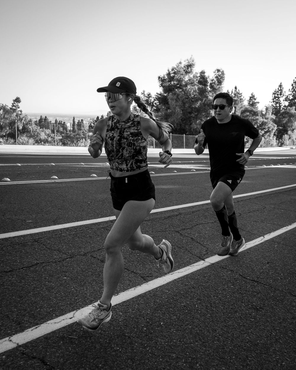 Black-and-white photo of two runners sprinting on a road with trees in the background.