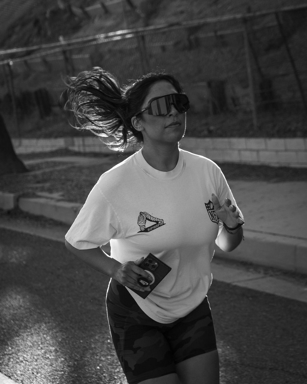 Black-and-white photo of a runner in a T-shirt and shorts jogging with ponytail swinging.