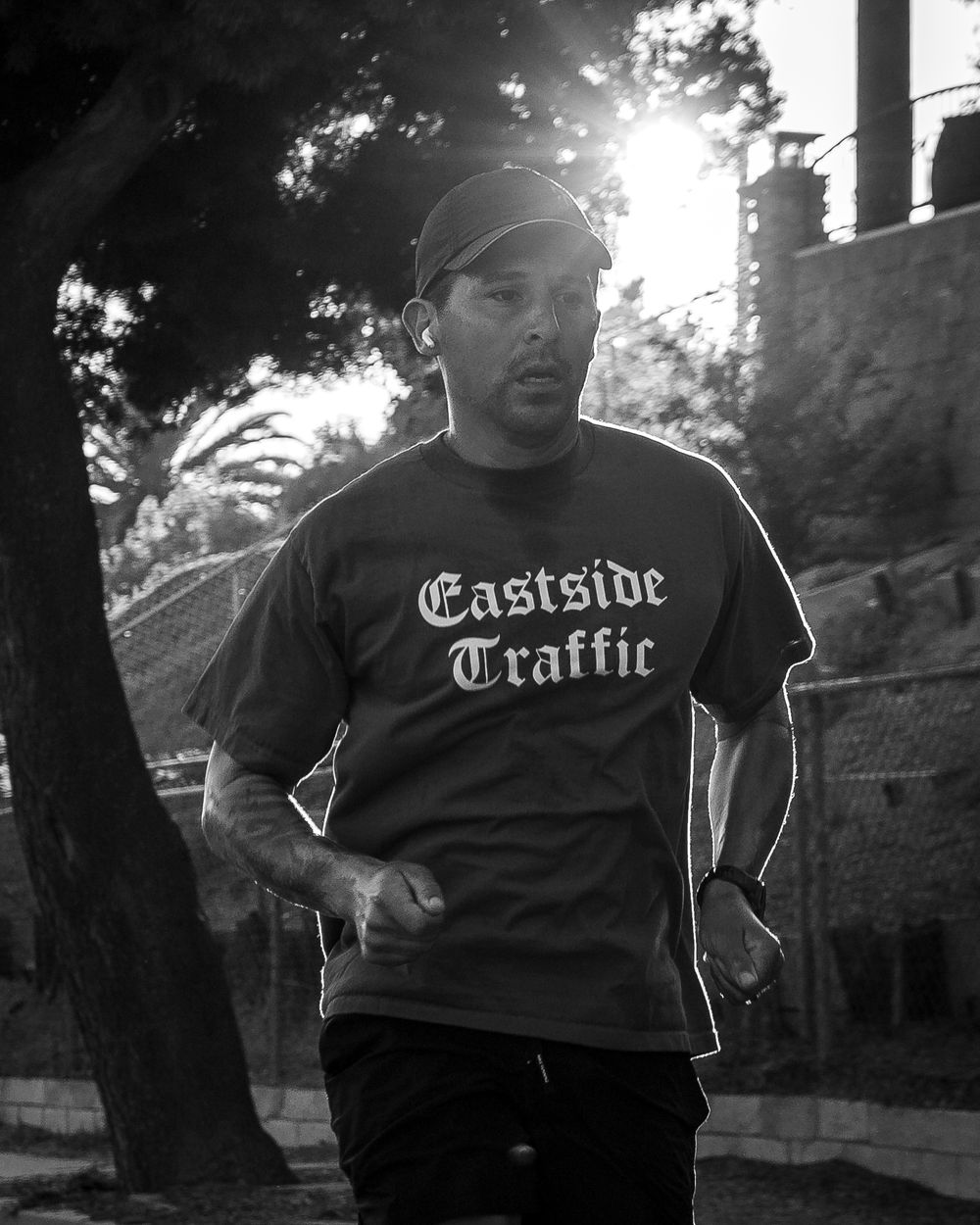 Black-and-white photo of a runner in an “Eastside Traffic” shirt jogging past trees at sunset.
