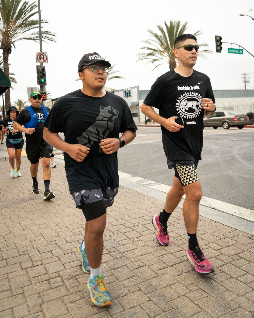 Group of runners in athletic gear jogging down a palm-lined city street during a race.