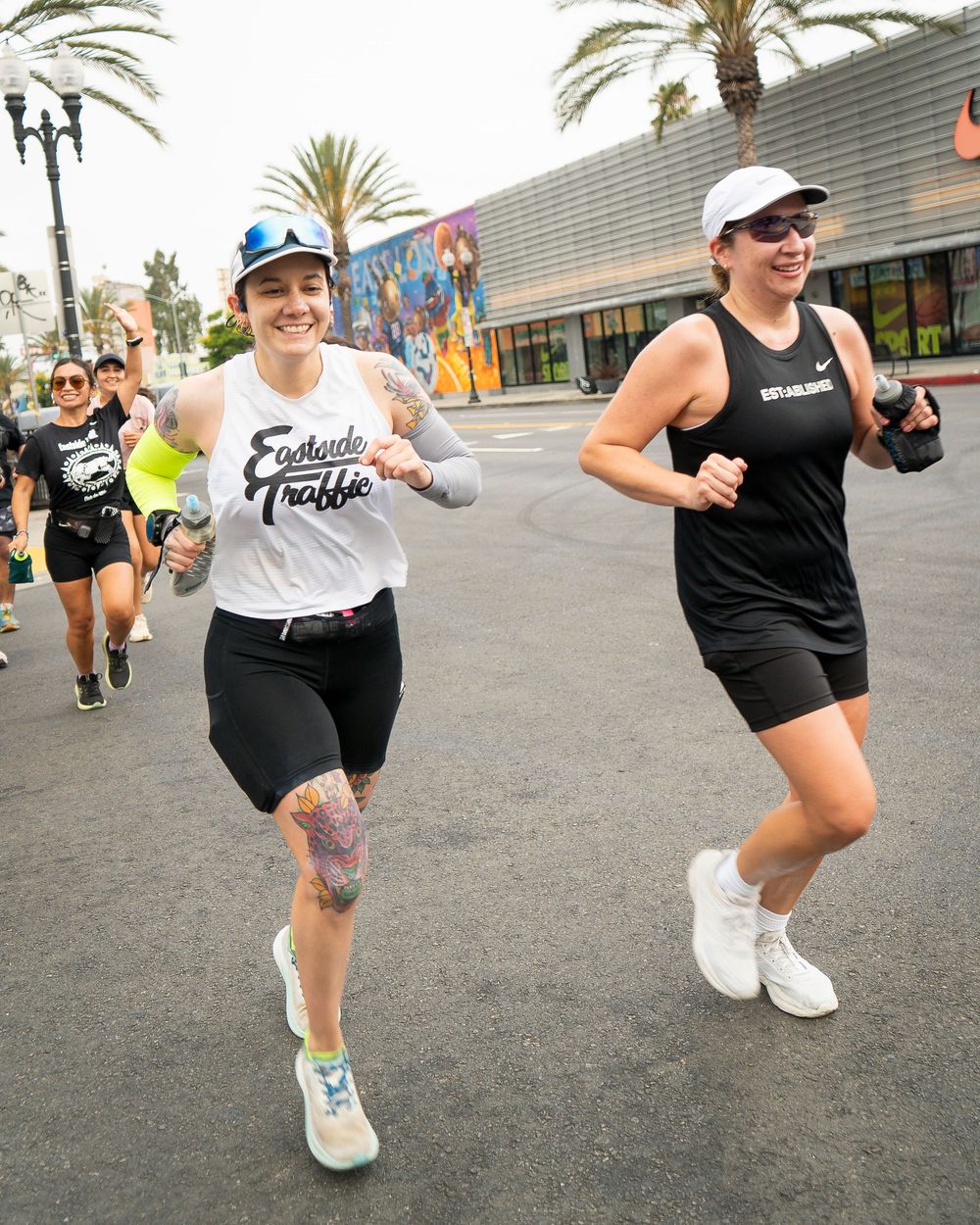 Group of runners in athletic gear jogging down a palm-lined city street during a race.
