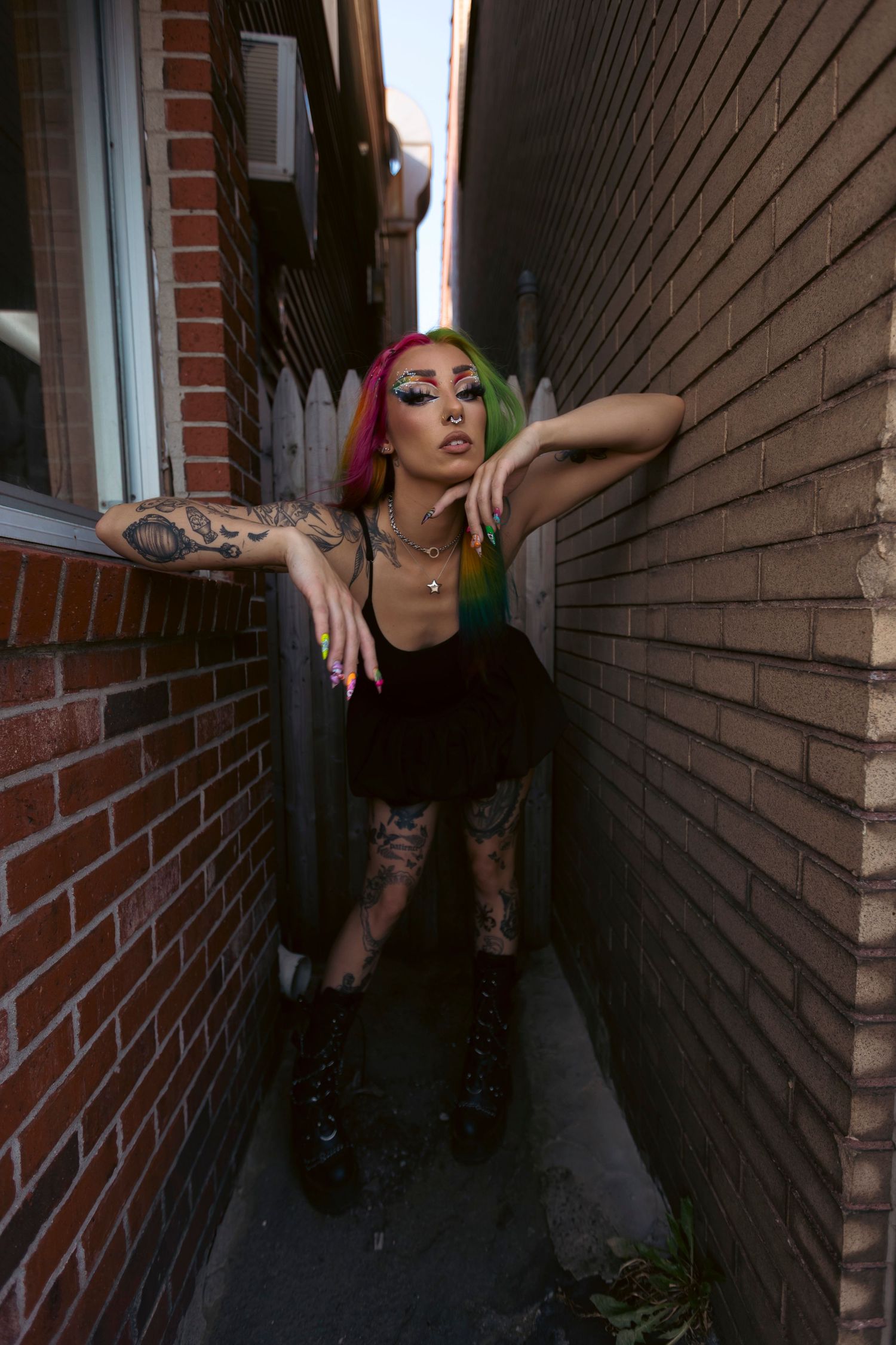 A dramatic fashion portrait in a narrow alleyway showing pink hair, tattoos, platform boots and edgy urban style.