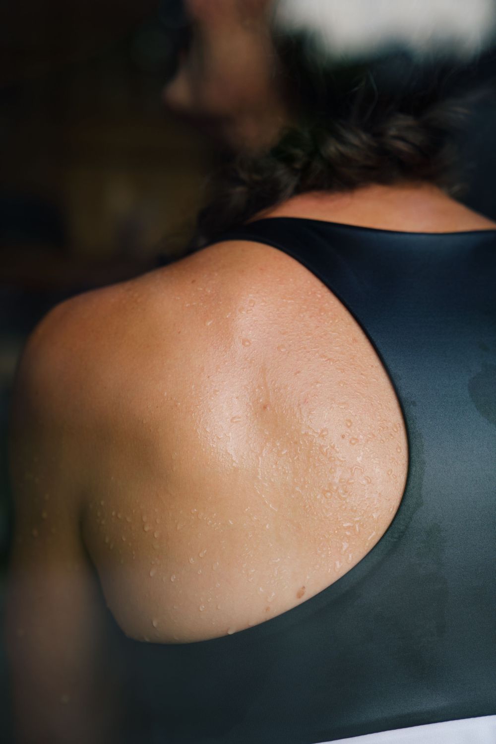 Close-up photo of a bare shoulder in a black tank top showing smooth skin texture in soft lighting.