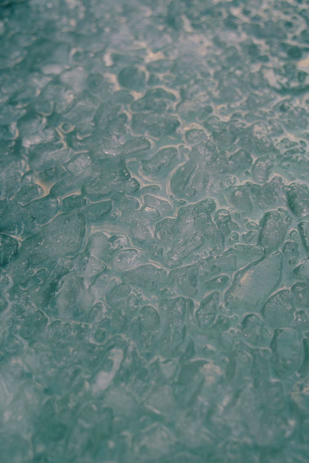 Abstract pattern of frozen water droplets on glass creates a textured teal and gray surface with organic shapes.