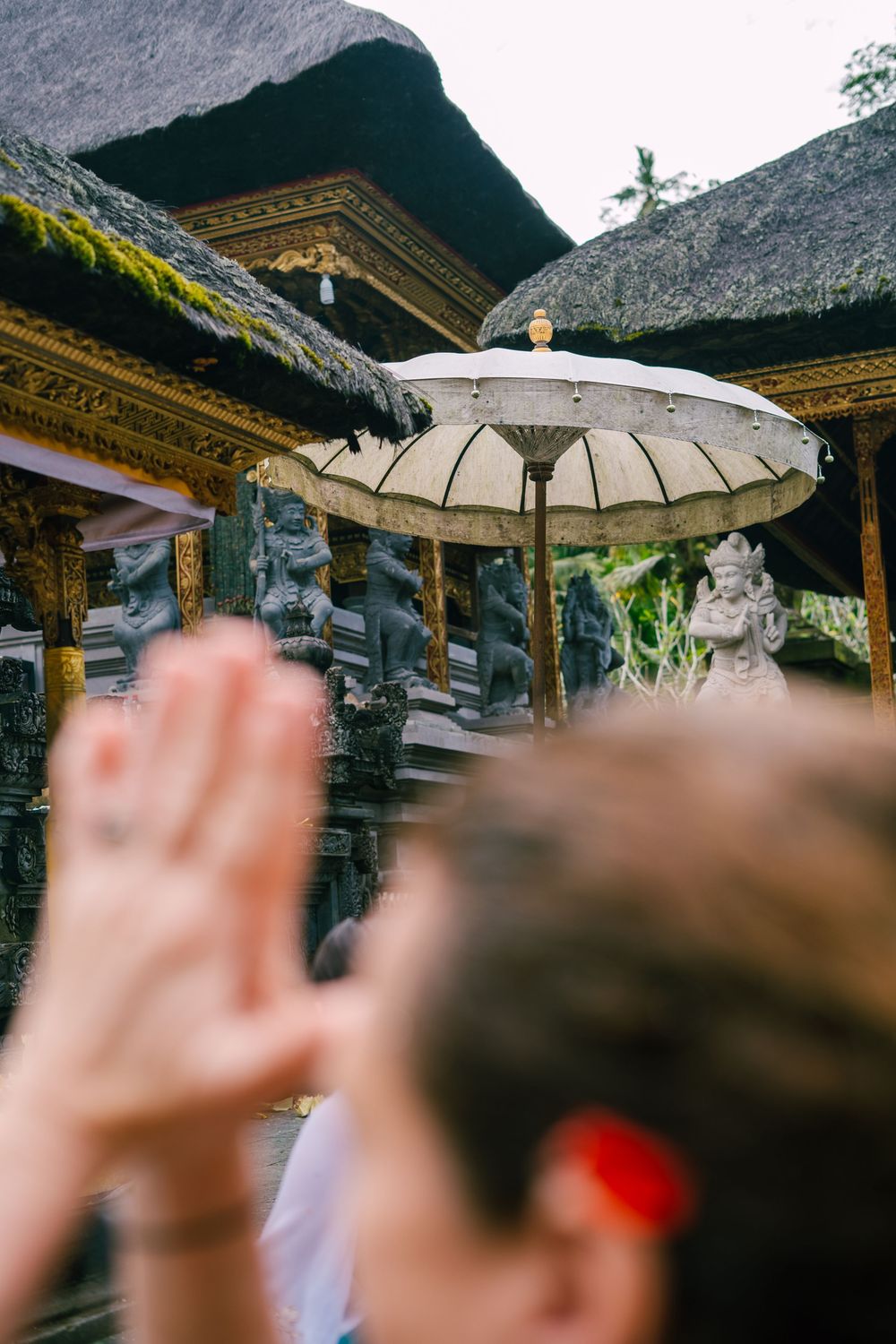 Traditional Balinese temple architecture with thatched roofs and ornate decorations under a white ceremonial umbrella.