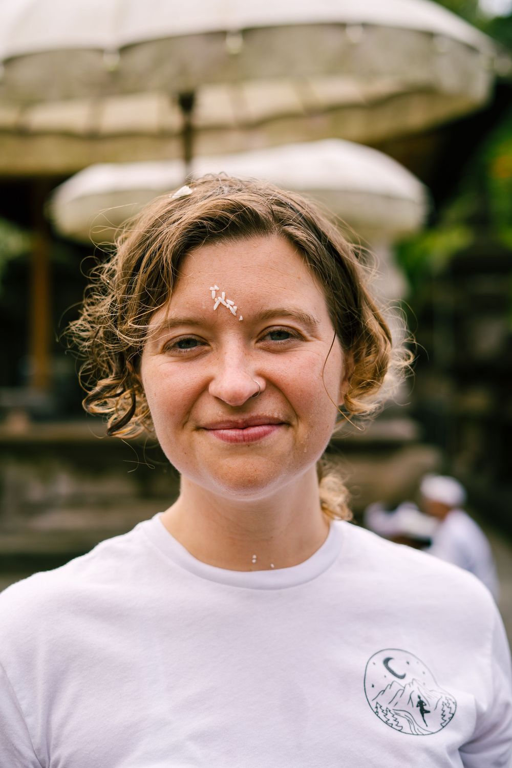 Person wearing white t-shirt with small logo smiling at camera.