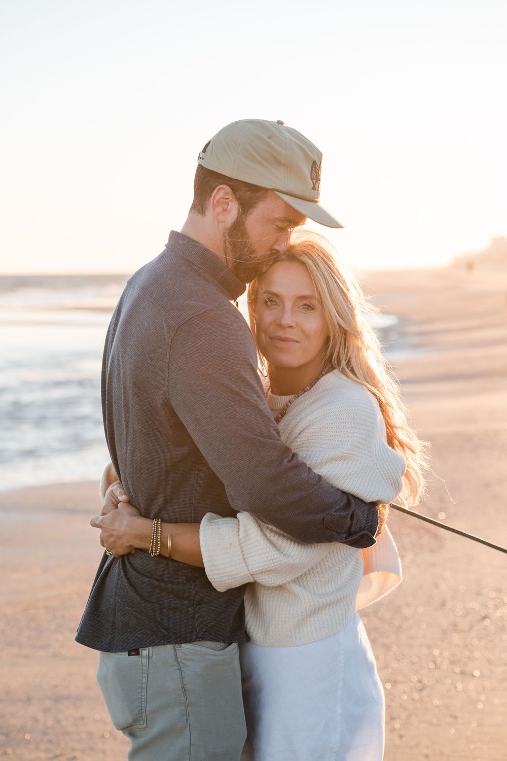 Couple embracing on a beach during sunset in casual attire.