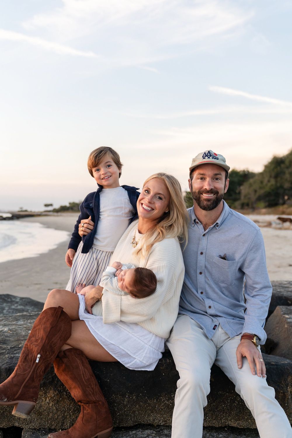 Family sitting together on rocks at the beach during golden hour with ocean waves in the background.