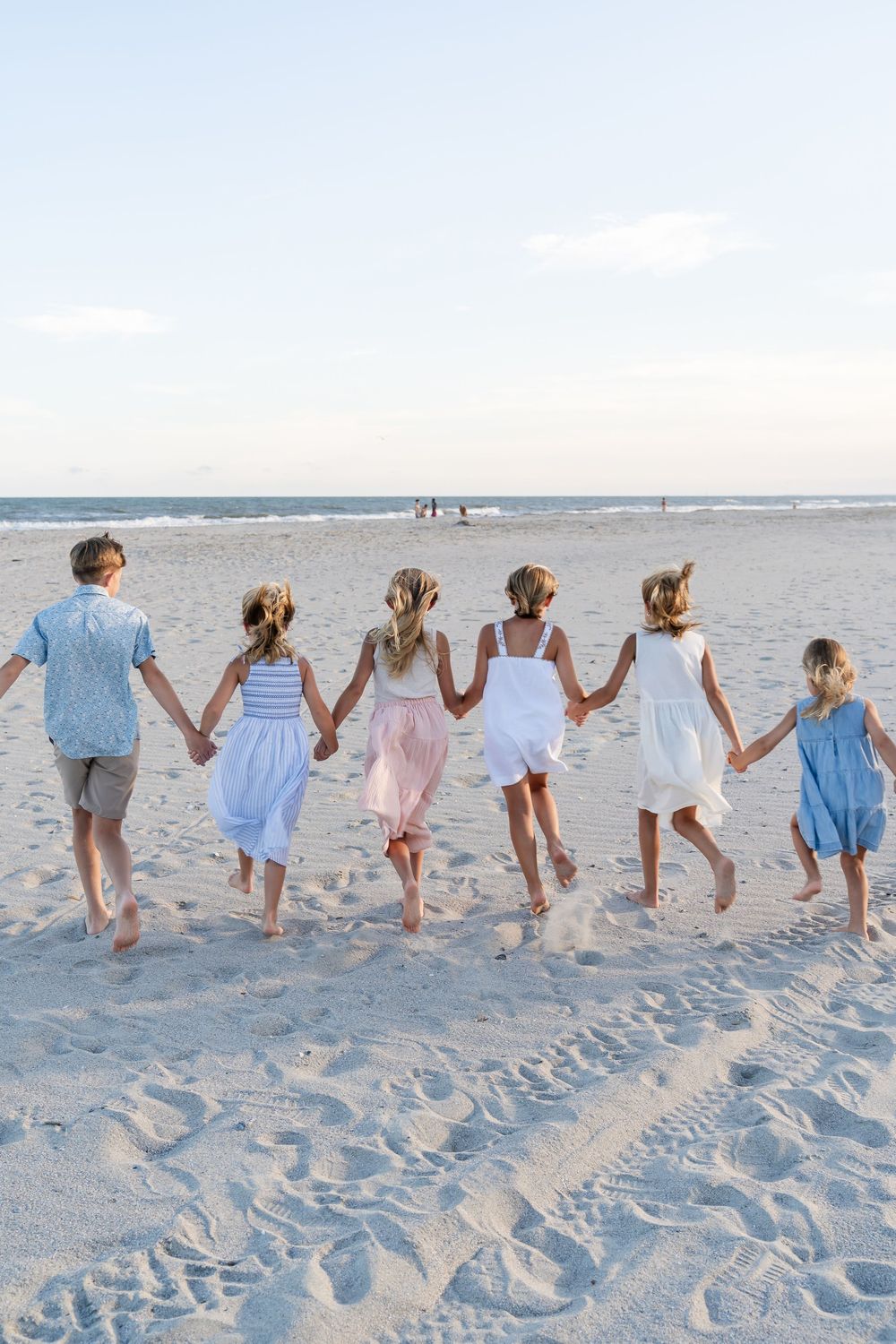 Group holding hands while walking along beach at sunset in coordinated outfits.