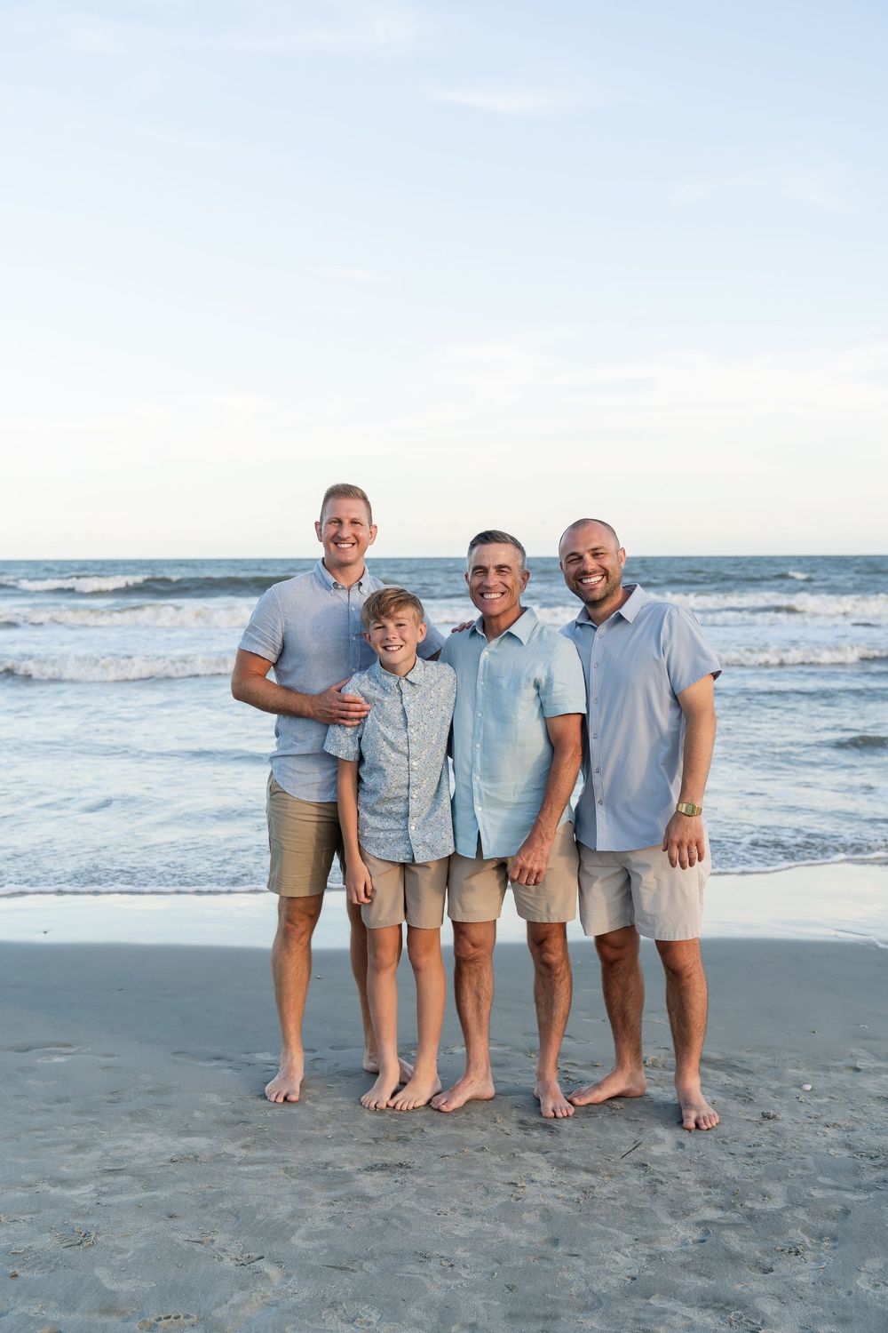 Small group wearing coordinating light blue and white outfits standing together on beach sand.