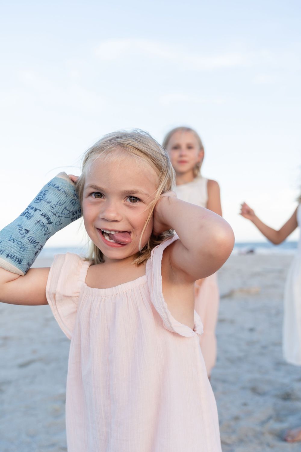 Child in pink dress playing and posing playfully on beach.