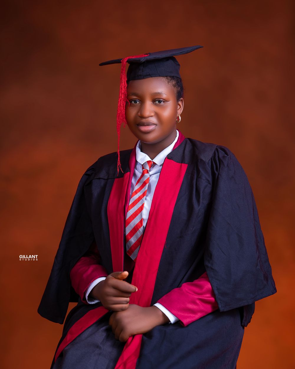 Professional graduation photo with traditional cap and gown against warm brown background.
