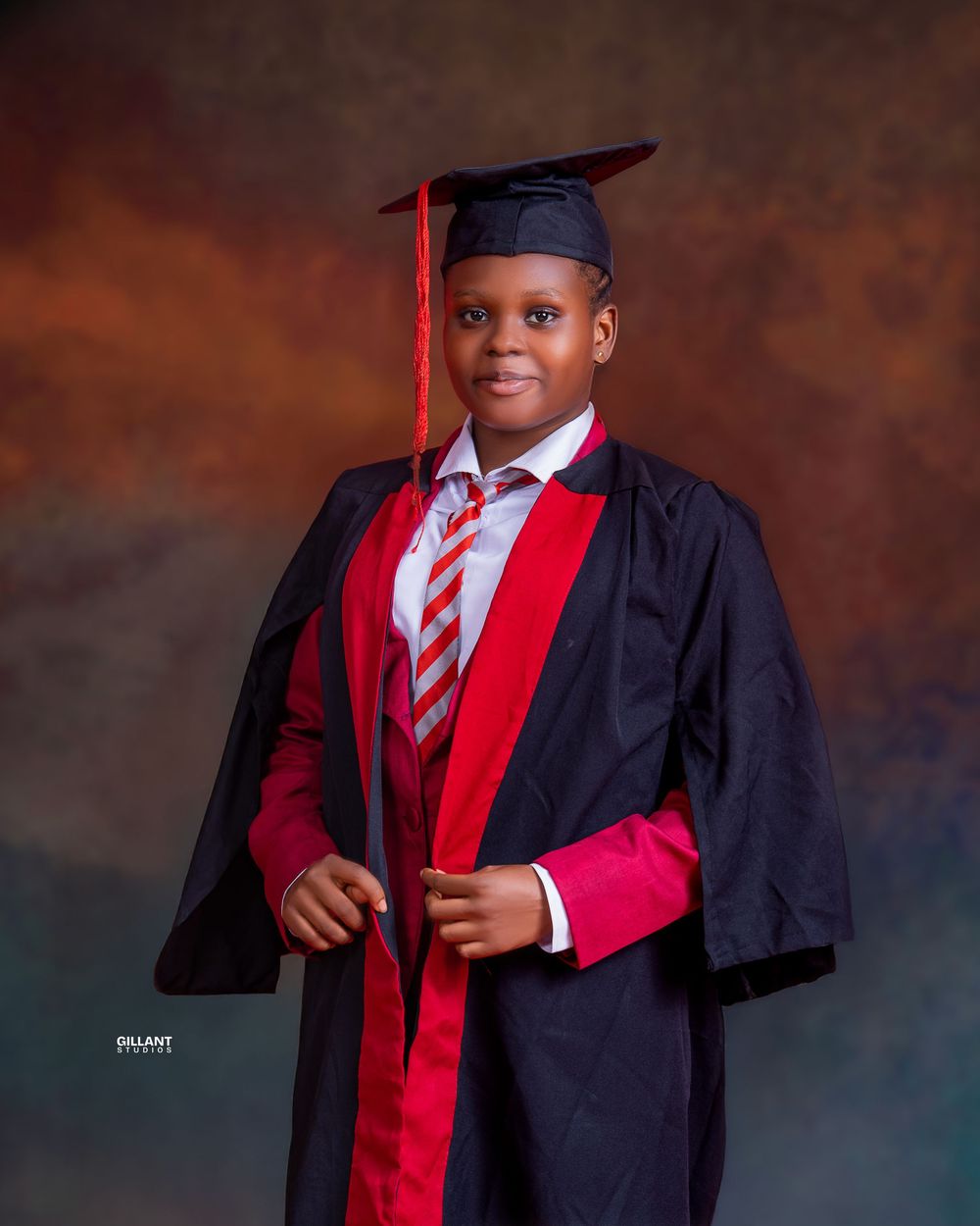 Studio graduation portrait featuring academic dress with red and navy colors against textured backdrop.