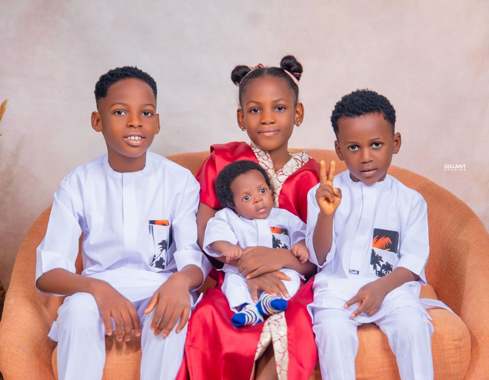 Four siblings in matching white outfits pose together on orange chair.