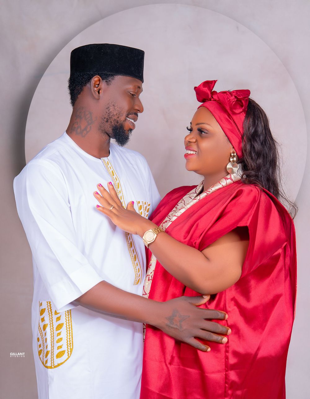 Loving couple in traditional white and red attire share intimate moment against neutral backdrop.
