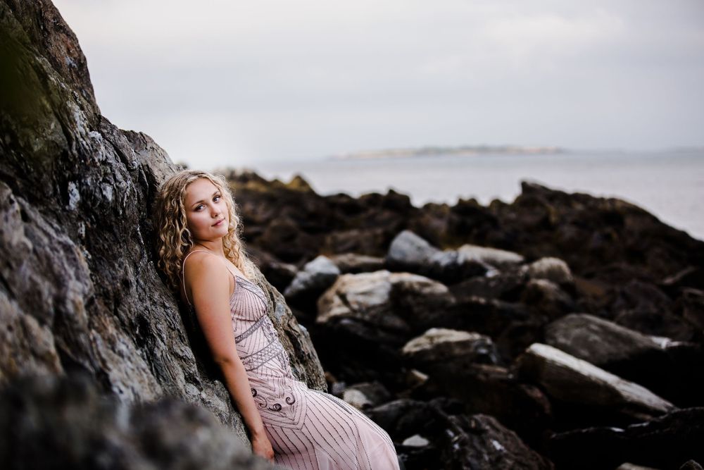 Portrait session on rocky coastal terrain with dramatic overcast sky in background.