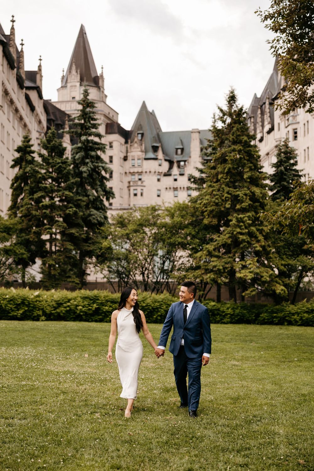 A couple walks hand in hand on the lawn in front of the magnificent Chateau Fairmont hotel in Quebec City.