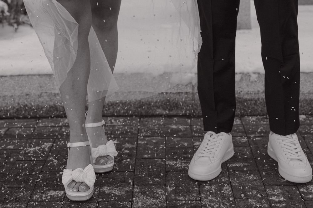 A black and white photo showing the feet of a wedding couple wearing white shoes on a speckled ground.