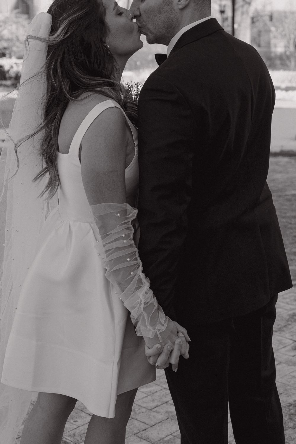 A romantic black and white wedding photo showing a couple sharing a tender kiss while holding hands.