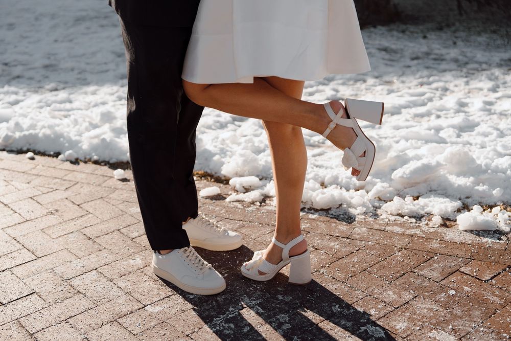 Closeup of feet showing silver heels and dress shoes on brick pavement with snow in background.