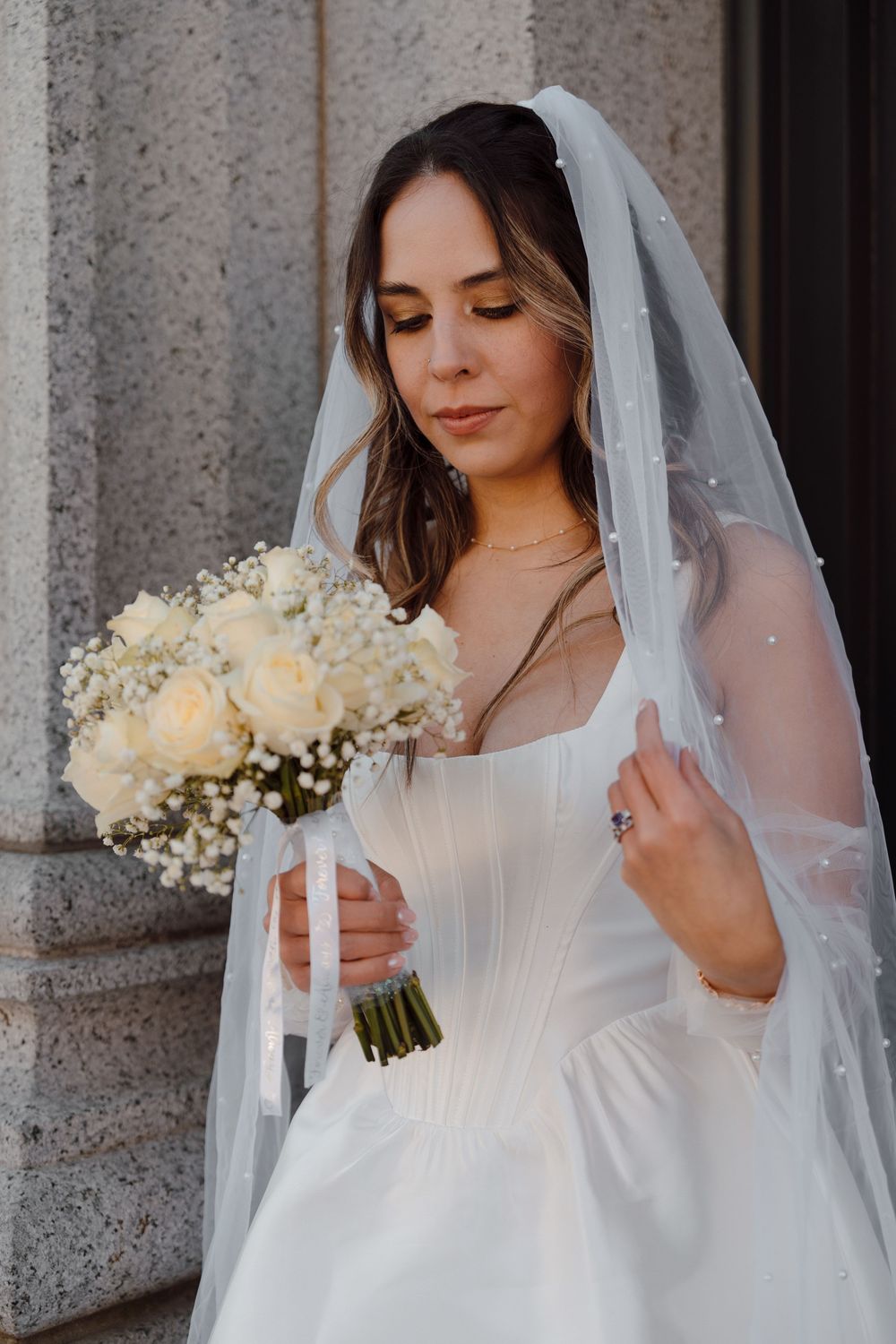 Four bridal portraits of a bride in white dress and veil holding an elegant bouquet of ivory roses against stone columns.