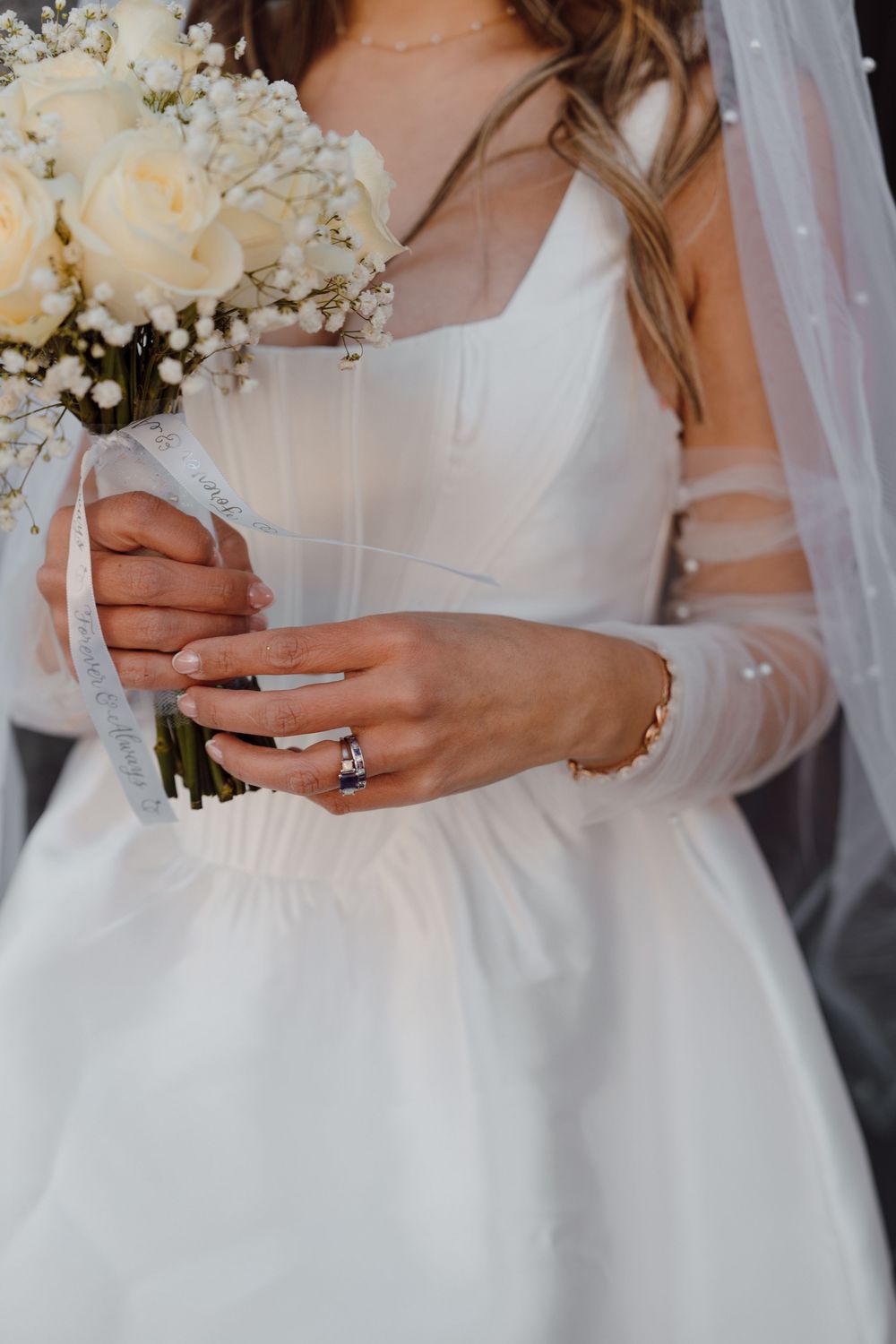 A close-up view of white bridal bouquet with roses held against an elegant wedding dress.