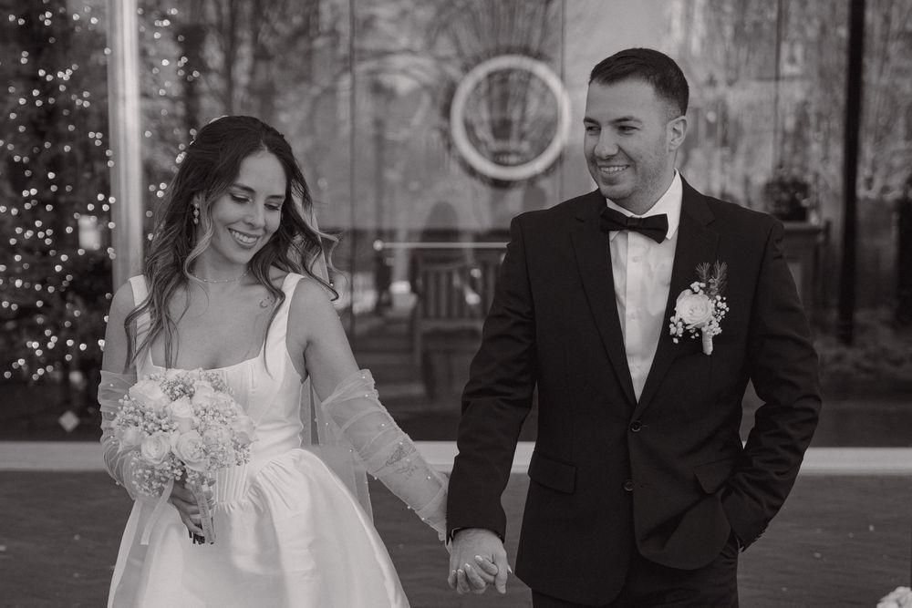 A black and white wedding photo of a couple holding hands, with the bride in a gown and groom in a tuxedo.