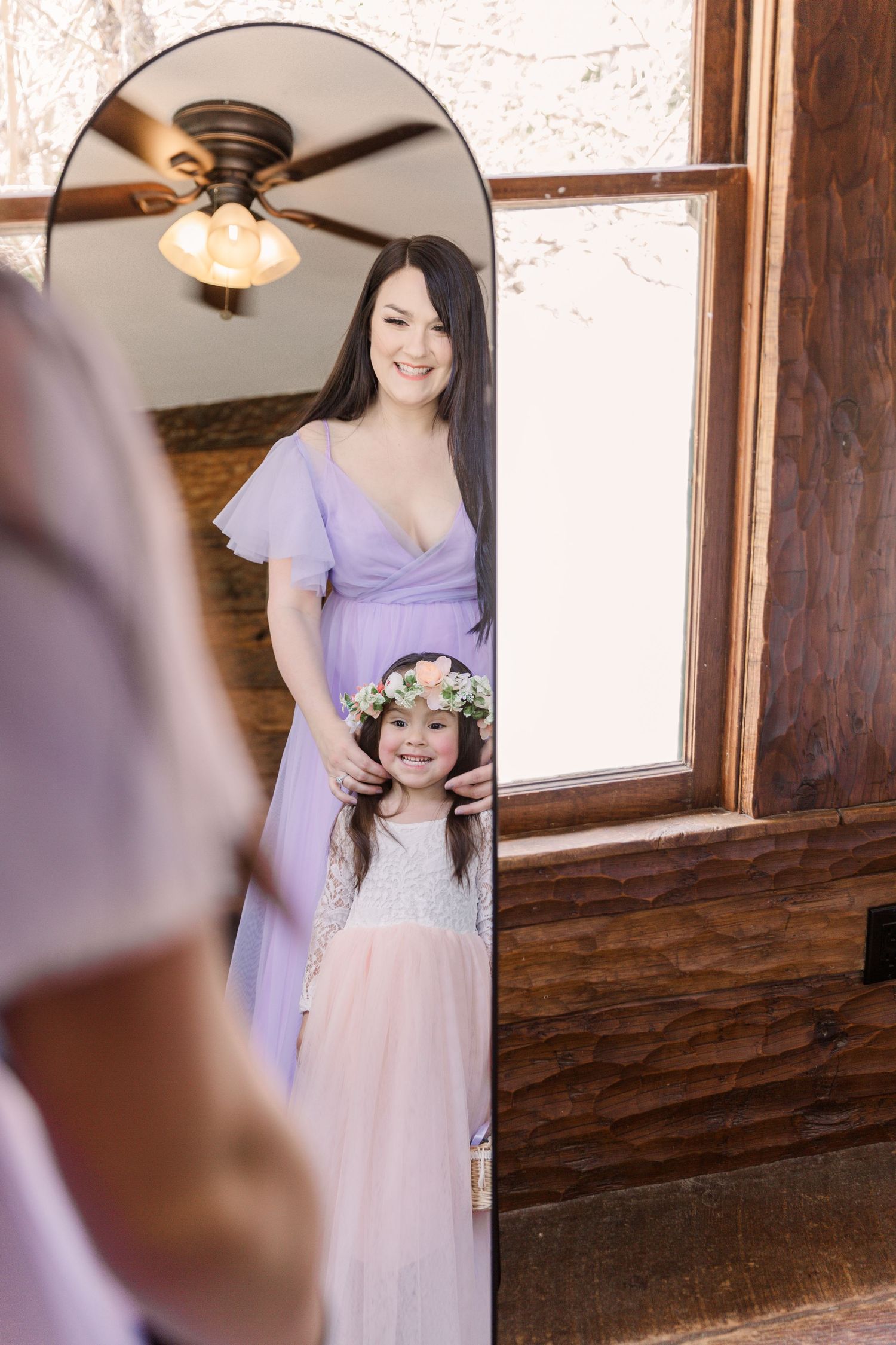 Bridesmaids in lavender dresses getting ready in a rustic wood-paneled room with natural lighting.