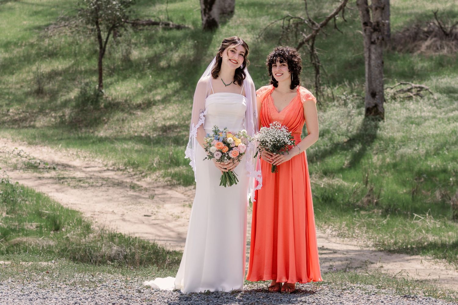 Bridesmaids in coral and white dresses posing together on an outdoor path surrounded by greenery.