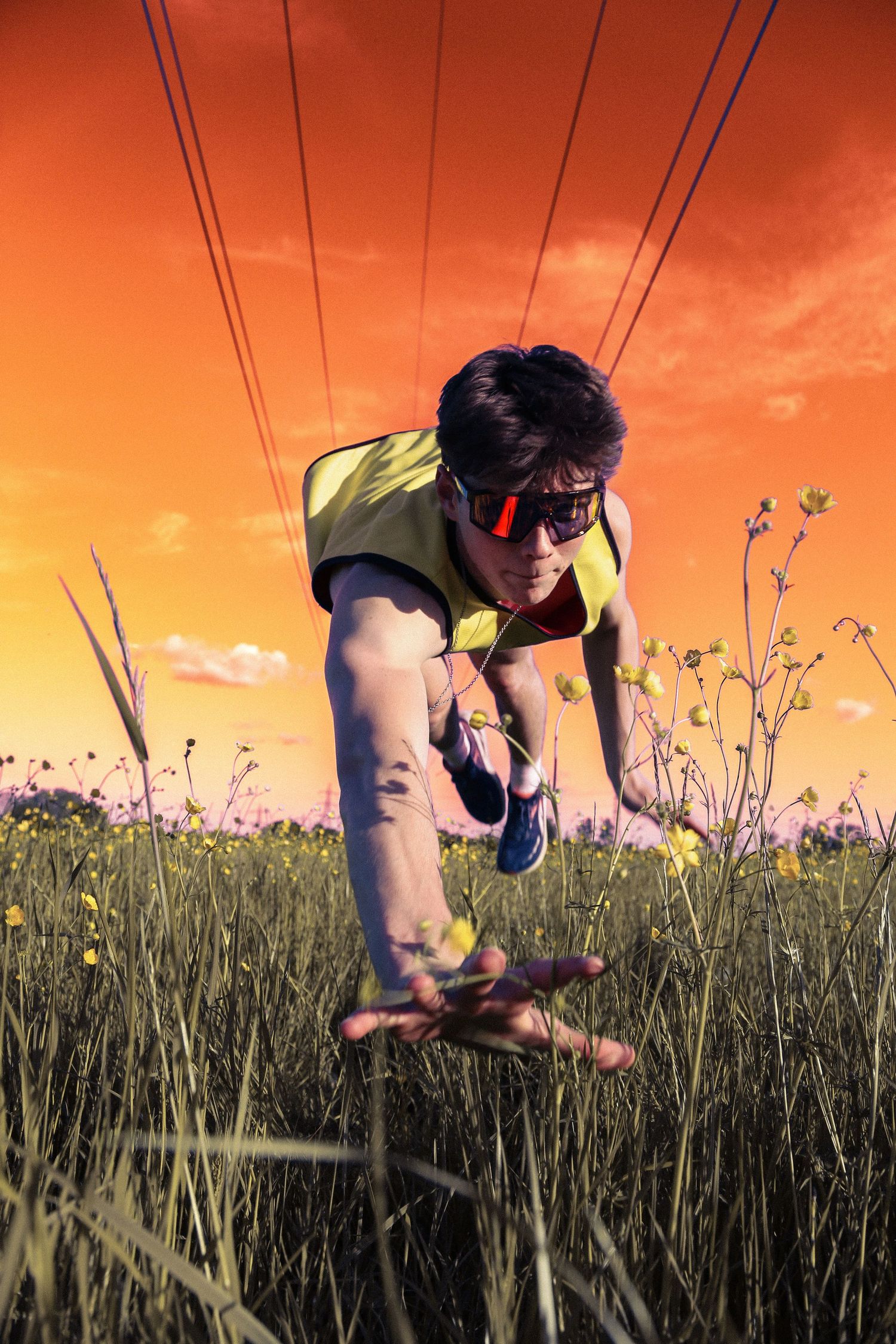 Athletic figure leaping through wildflower field against dramatic orange sky.